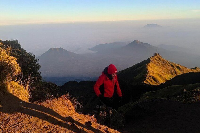 A person in a red jacket hiking on a mountain trail with a view of distant mountains. 1