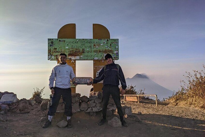 Two people standing in front of a signpost with a mountain in the background. 4