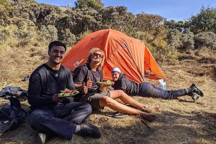 Two people sitting outdoors with a red tent in the background. 3