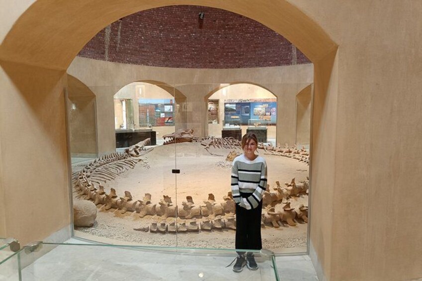A person standing in a museum with ancient artifacts displayed in the background. 2