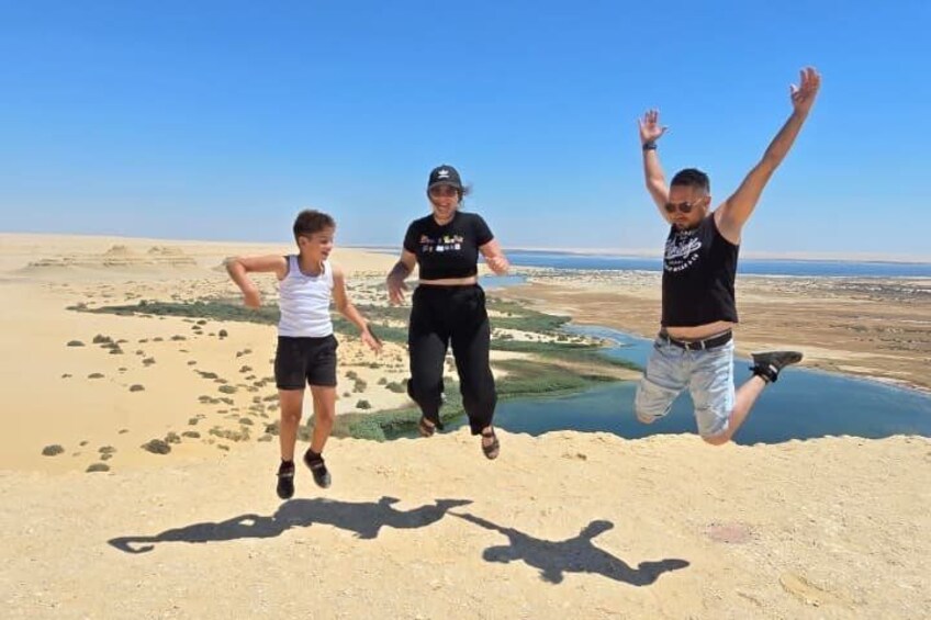 Three people jumping on a sandy beach with a body of water and a clear sky in the background. 5