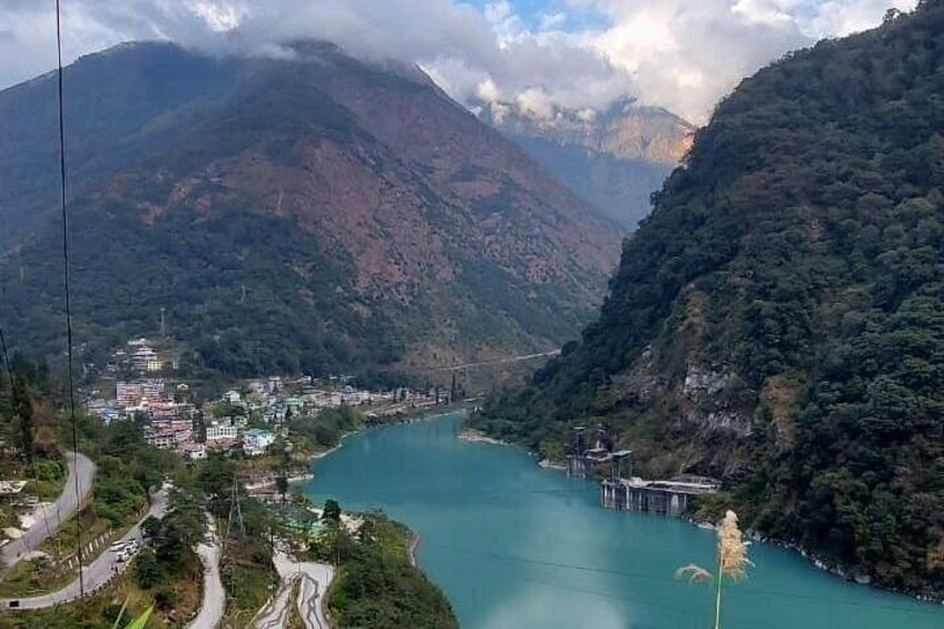 A river winding through a mountainous landscape with a town on one side and a bridge on the other. 3