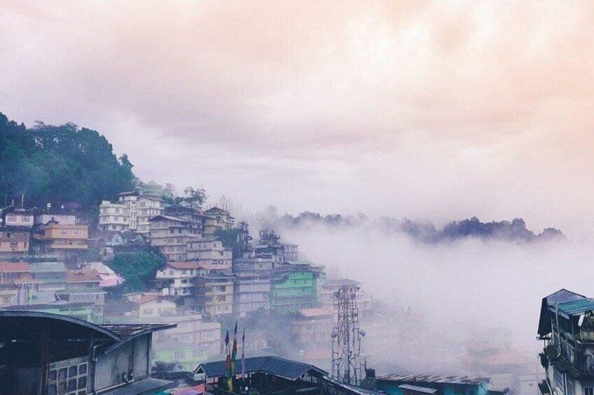 A mountainous village with buildings perched on a hillside, surrounded by mist. 2
