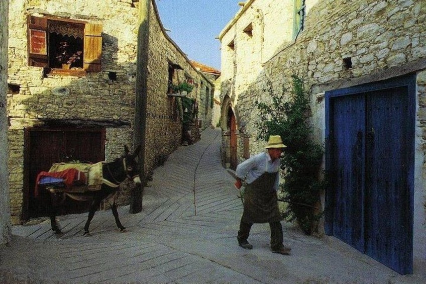 Eine schmale Gasse mit Steinhäusern, einem Eselswagen und einem Mann in traditioneller Kleidung. 2