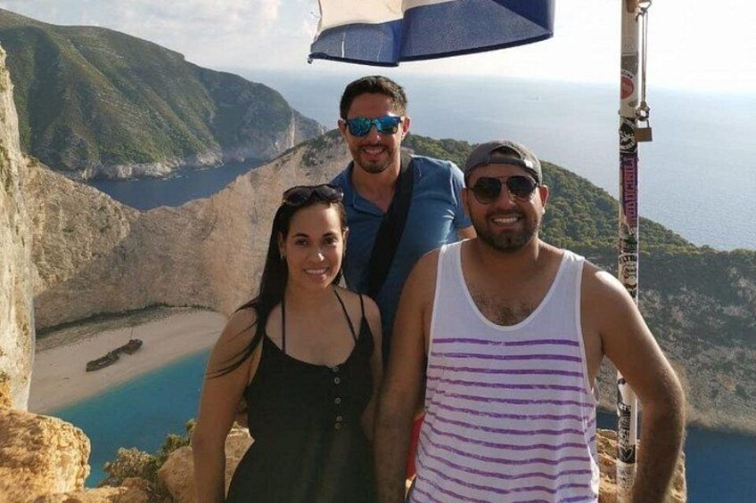 Drei Personen stehen auf einer Klippe mit Blick auf eine Küstenlandschaft mit Strand und Felsen. 3