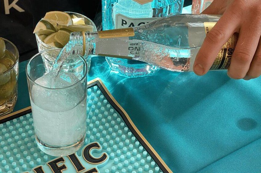 A hand pouring a clear liquid from a bottle into a glass with ice. 3