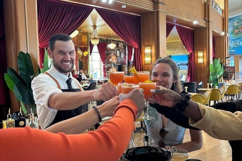A bar setting with a bartender and customers toasting with drinks. 1