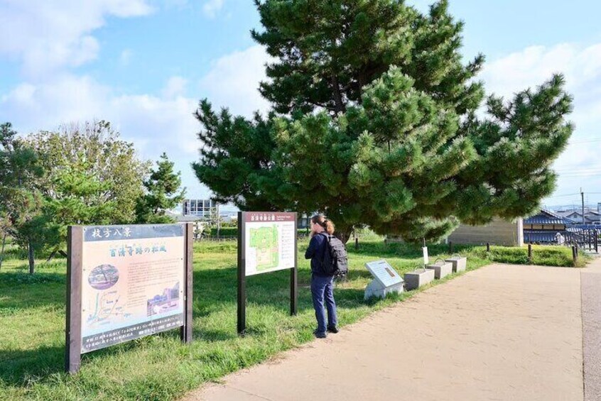 Een persoon staat bij een bord in een park met bomen en een pad. 2