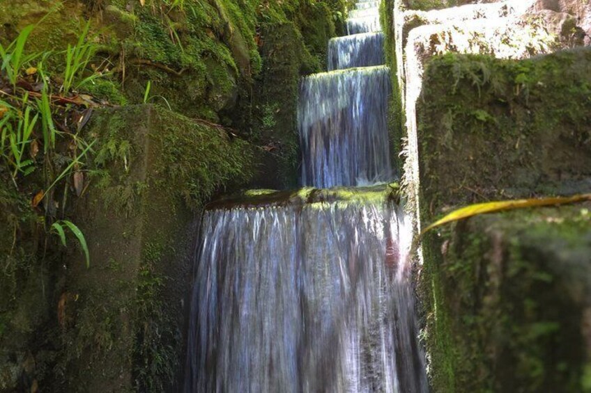 A multi-tiered waterfall surrounded by moss-covered rocks and greenery. 2
