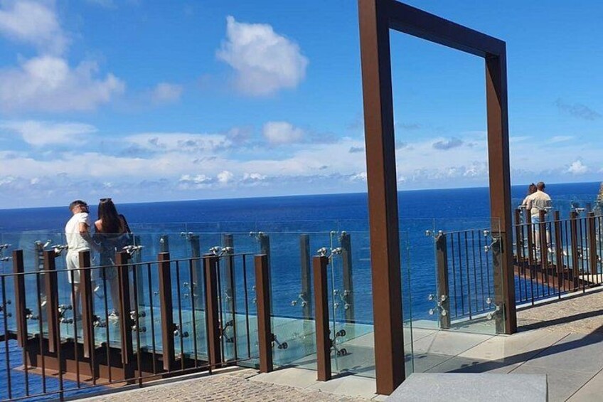 A glass railing overlooking the ocean, with people walking along the promenade. 2
