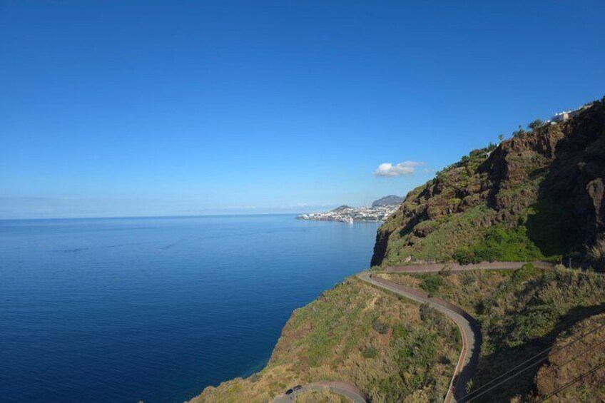 A coastal road winding along a cliffside with a view of the ocean and distant cityscape. 5