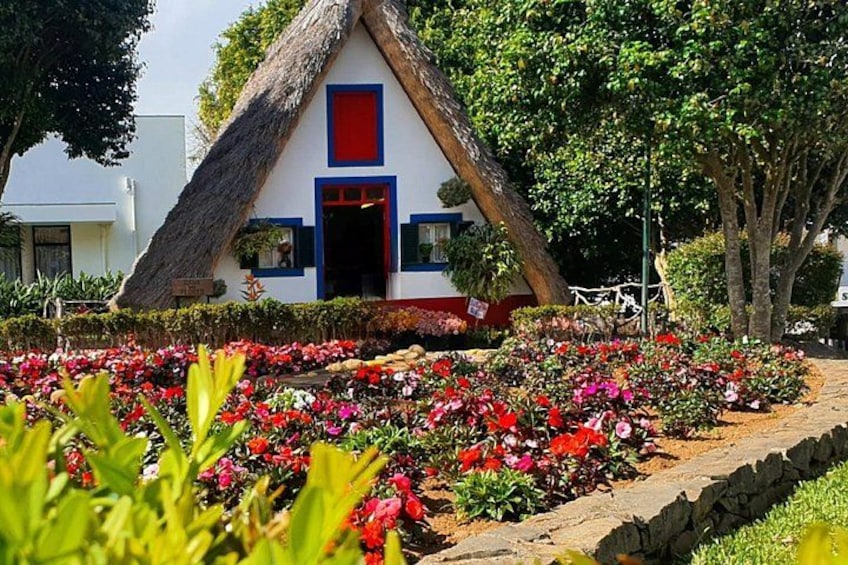 A thatched-roof house with a red door, surrounded by a vibrant flower garden. 1