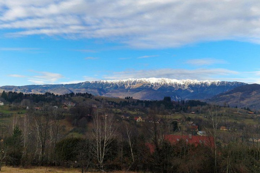 A mountainous landscape with snow-capped peaks, a valley with scattered houses, and a clear blue sky. 3