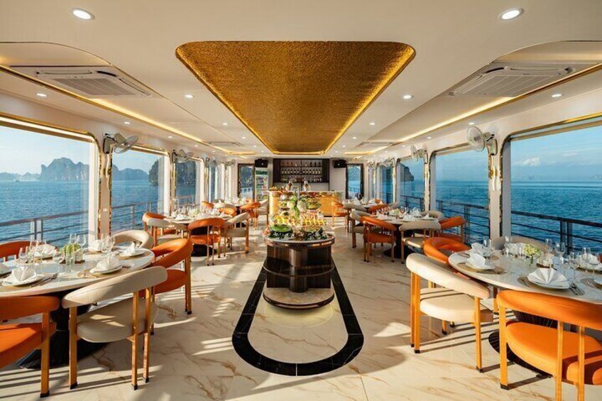 Un espace de restauration luxueux, doté de tables et de chaises, d’un bar central et de grandes fenêtres offrant une vue sur l’océan. 1