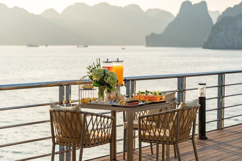 Une table dressée avec des boissons, des fleurs et de la nourriture, sur un bateau offrant une vue sur la mer et les montagnes. 4