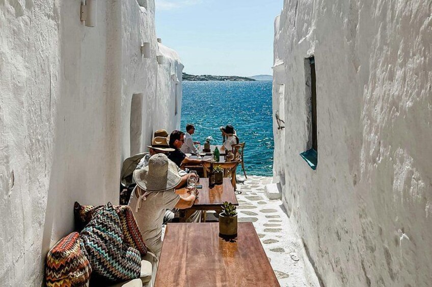 A narrow alley with white-washed walls, a wooden table, and a view of the sea. 5
