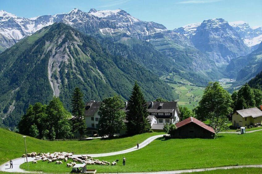 A mountainous landscape with a green valley, houses, and a herd of sheep. 3