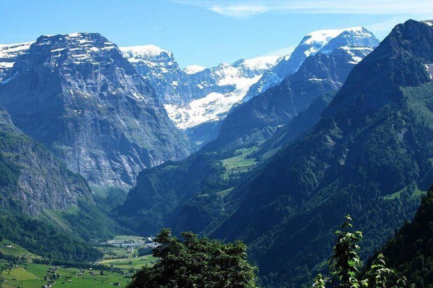 A mountainous landscape with snow-capped peaks, dense green forests, and a valley. 4