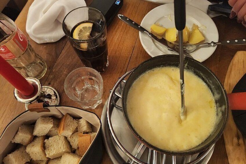 A fondue pot with cheese, a bottle of red wine, and bread on a table. 5