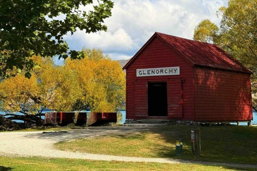 En rød lade med skiltet 'Glenorchy', adgang via en grussti, omgivet af træer med gule blade. 2