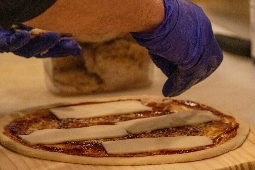 A person wearing gloves preparing a pizza with tomato sauce and cheese. 2