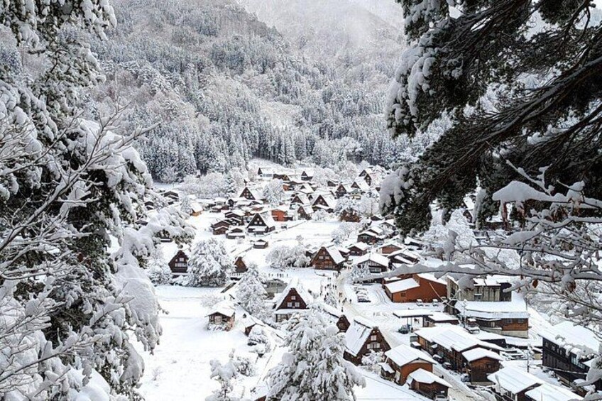 A snow-covered village with traditional houses, a river, and surrounding forest. 4