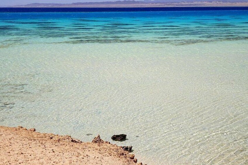 A clear turquoise sea with a sandy beach and a rocky outcrop. 3