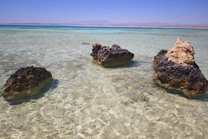 Clear turquoise water, three large rocks, and a distant mountain range. 5