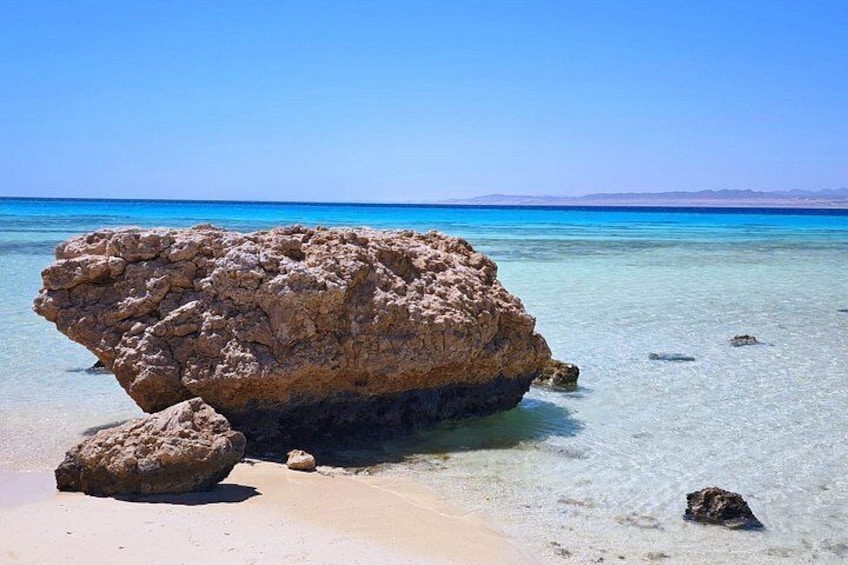 A large rock formation on a clear beach with calm turquoise waters. 4