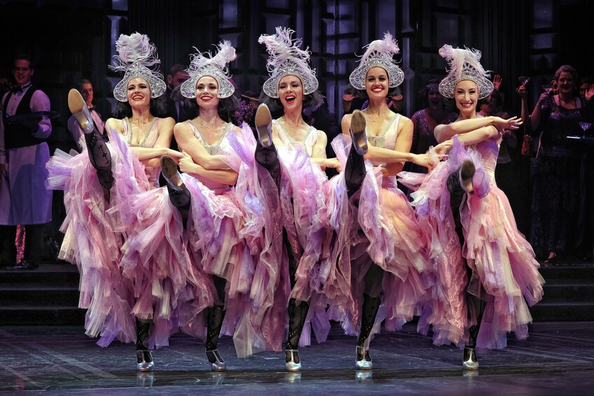 A group of dancers in pink tutus and silver hats performing on stage. 3