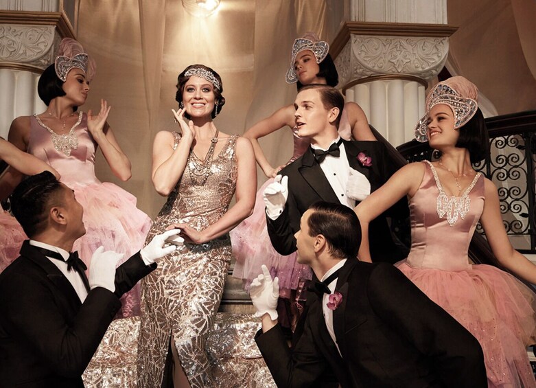 A group of people in formal attire, including dresses and suits, in an ornate room with decorative columns and a chandelier. 1