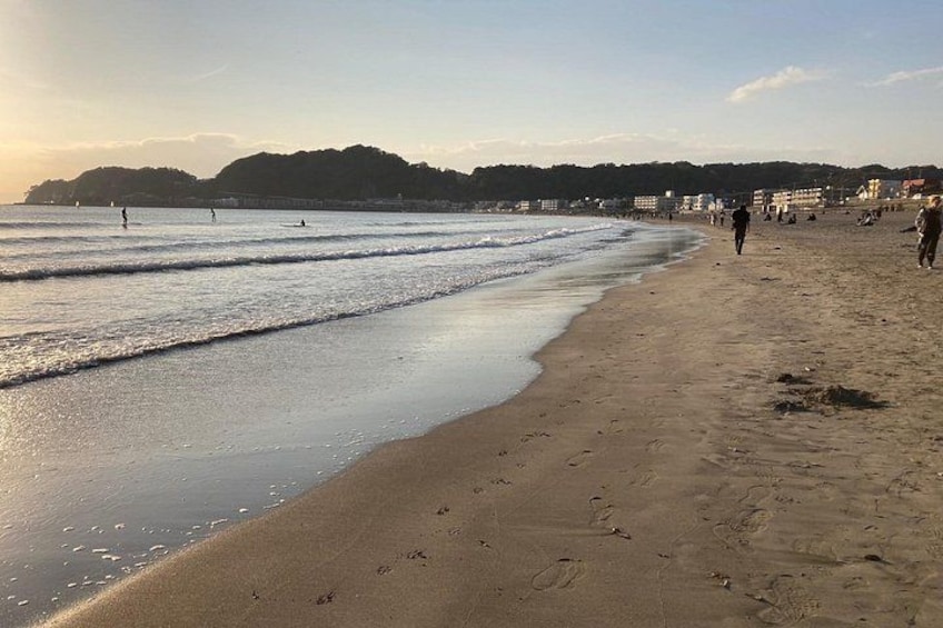 Une plage où l’on voit des gens se promener et nager, un rivage sablonneux et une colline au loin. 4