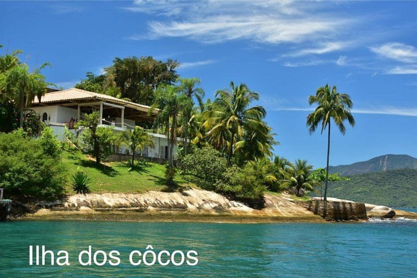 A coastal house with palm trees, clear blue water, and a mountainous background. 3
