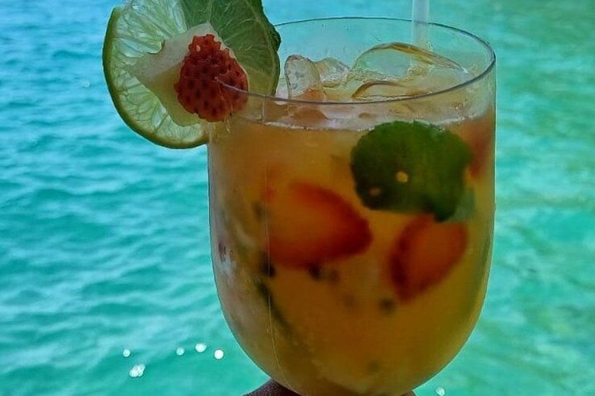 A tropical drink with fruit and a lime wedge, set against a turquoise sea backdrop. 2