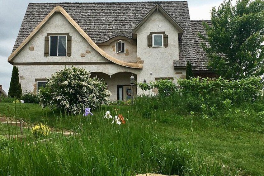 A two-story house with a sloped roof, surrounded by lush greenery and a flowering bush. 4