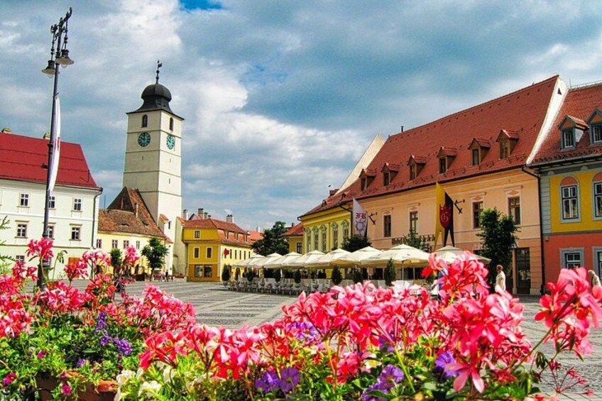 A town square with colorful flowers, a clock tower, and traditional buildings. 1