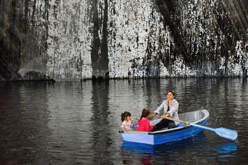 A boat with three people on a calm body of water, surrounded by a rocky cliff with white and black patterns. 4