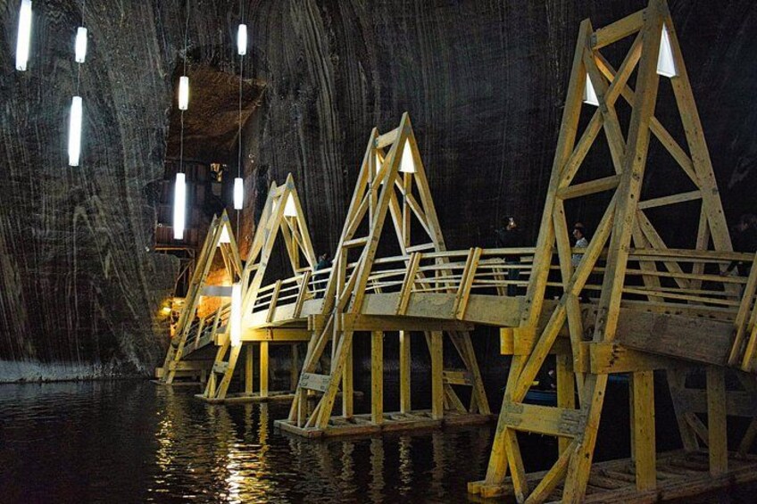 Wooden walkways over water in a cave-like setting with hanging lights. 5