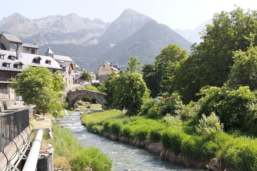 Un fiume serpeggia attraverso un villaggio con un ponte, circondato da montagne e vegetazione. 3