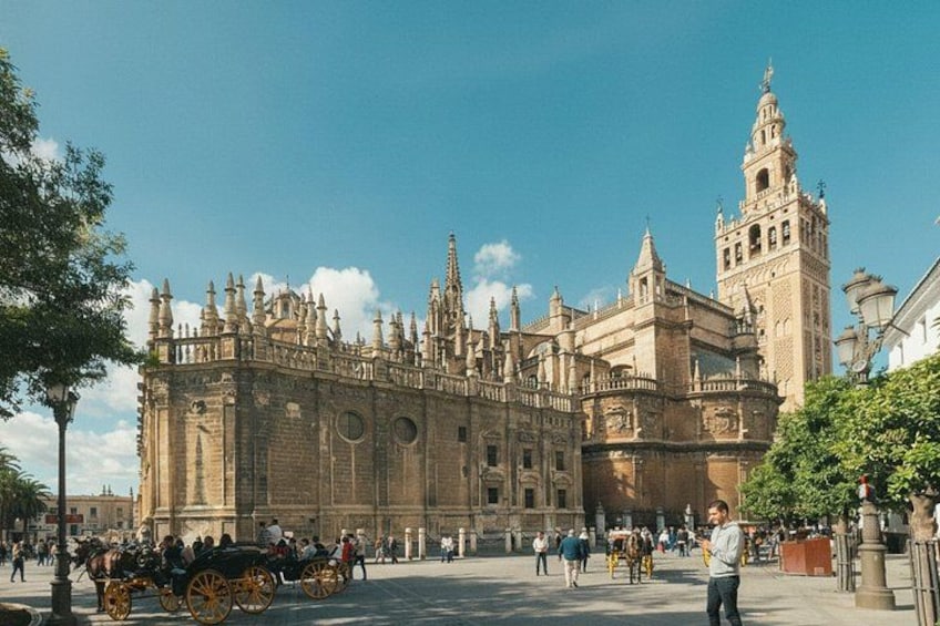 A historic building with intricate architecture, a clock tower, and a plaza with people and horse-drawn carriages. 3