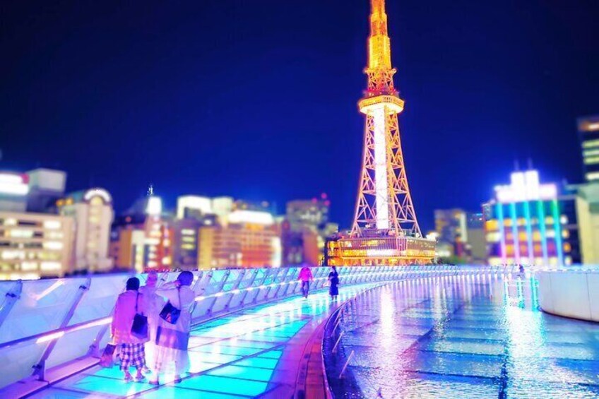 Una torre iluminada, con su reflejo en el agua, rodeada de edificios. 1
