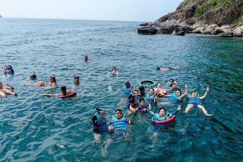 Personas flotando en el agua con chalecos salvavidas, un litoral rocoso y mar tranquilo. 2