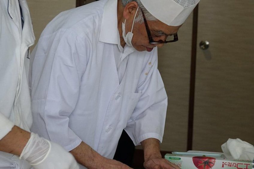 Una persona con bata y gorro blancos, posiblemente un cocinero, trabajando en un mostrador con una caja que tiene un diseño rojo y blanco. 3