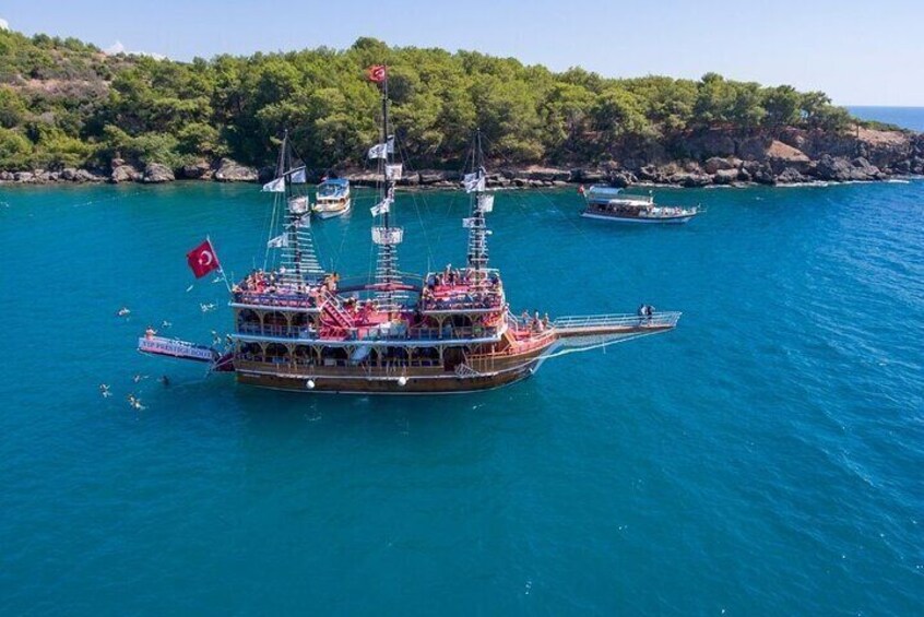 A large boat with multiple decks and flags, anchored in a turquoise sea with other boats in the background. 4