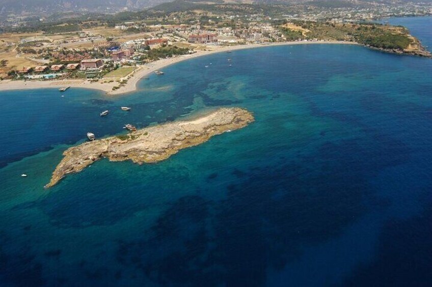 An aerial view of a coastal town with a sandy beach, clear blue waters, and a rocky outcrop. 2