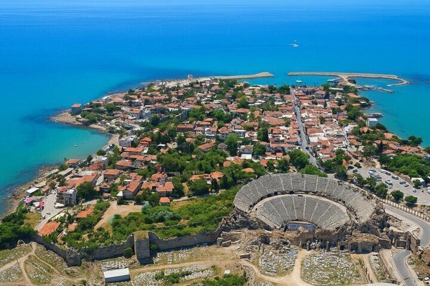 An aerial view of a coastal town with a historic amphitheater, clear blue waters, and a mix of residential and commercial buildings. 3