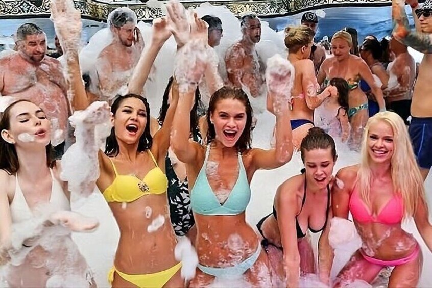A group of people in a beach setting, some wearing swimsuits and others in casual clothing, with water splashing around them. 5