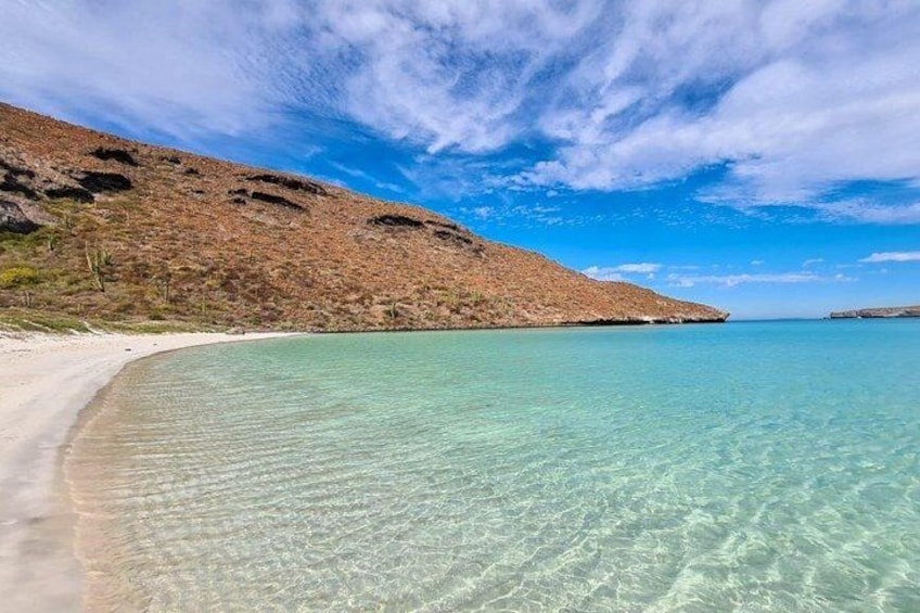 A beach with clear turquoise water, sandy shore, and a rocky hillside. 5