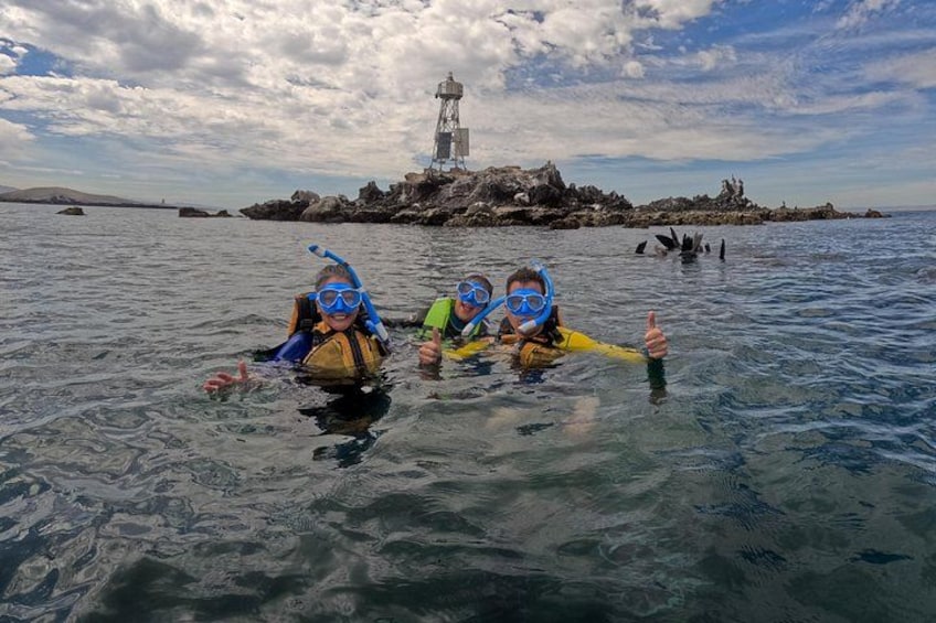 Two people snorkeling in clear water with a rocky island and lighthouse in the background. 1