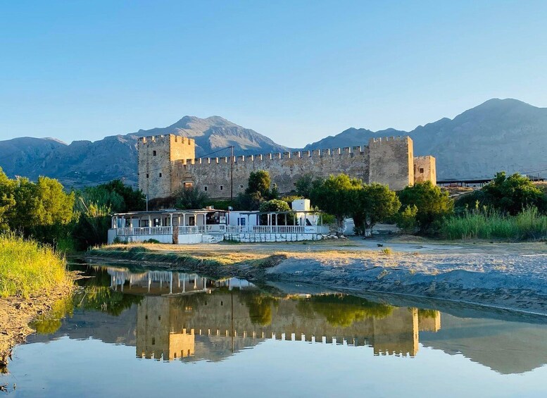 A castle with a reflection in a calm body of water, surrounded by greenery and mountains. 2